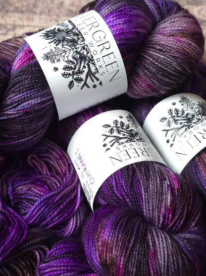 Three skeins of variegated yarn in deep purple and black shades with white paper labels.