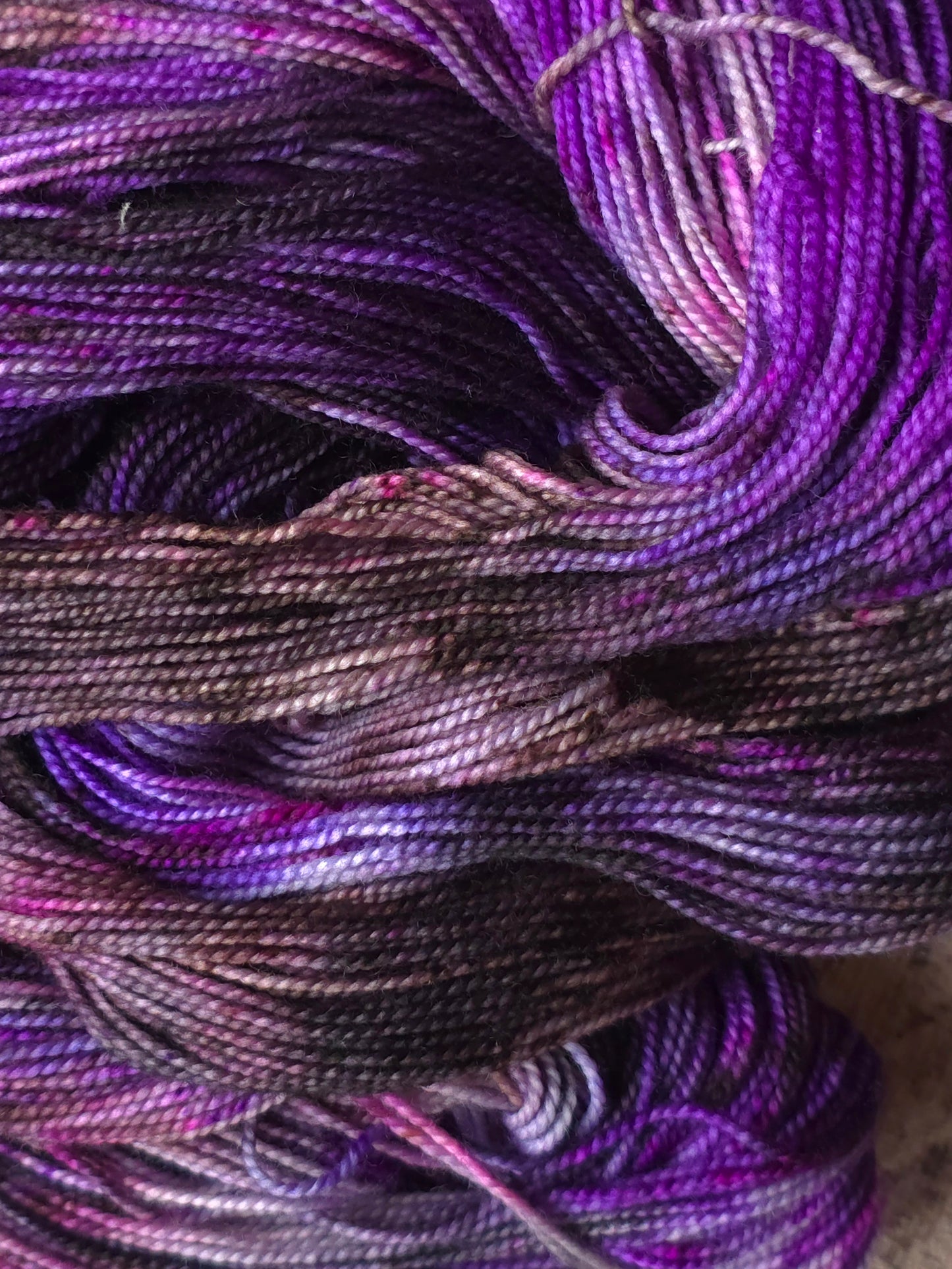 Close-up of variegated yarn with a color-shifting effect, showing transitions between deep purple, violet, magenta, and dark charcoal gray.