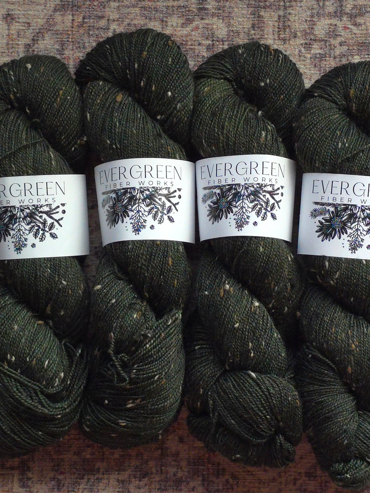 Four skeins of dark green yarn with 'Evergreen Yarn Works' labels on a textured surface.