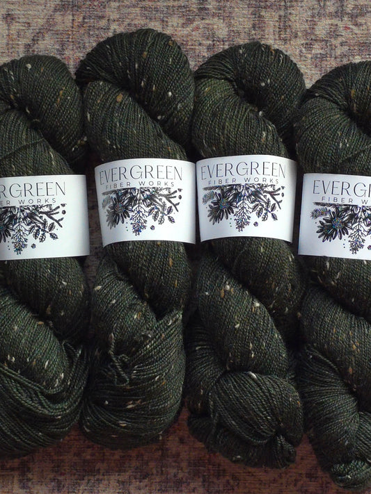 Four skeins of dark green yarn with 'Evergreen Yarn Works' labels on a textured surface.
